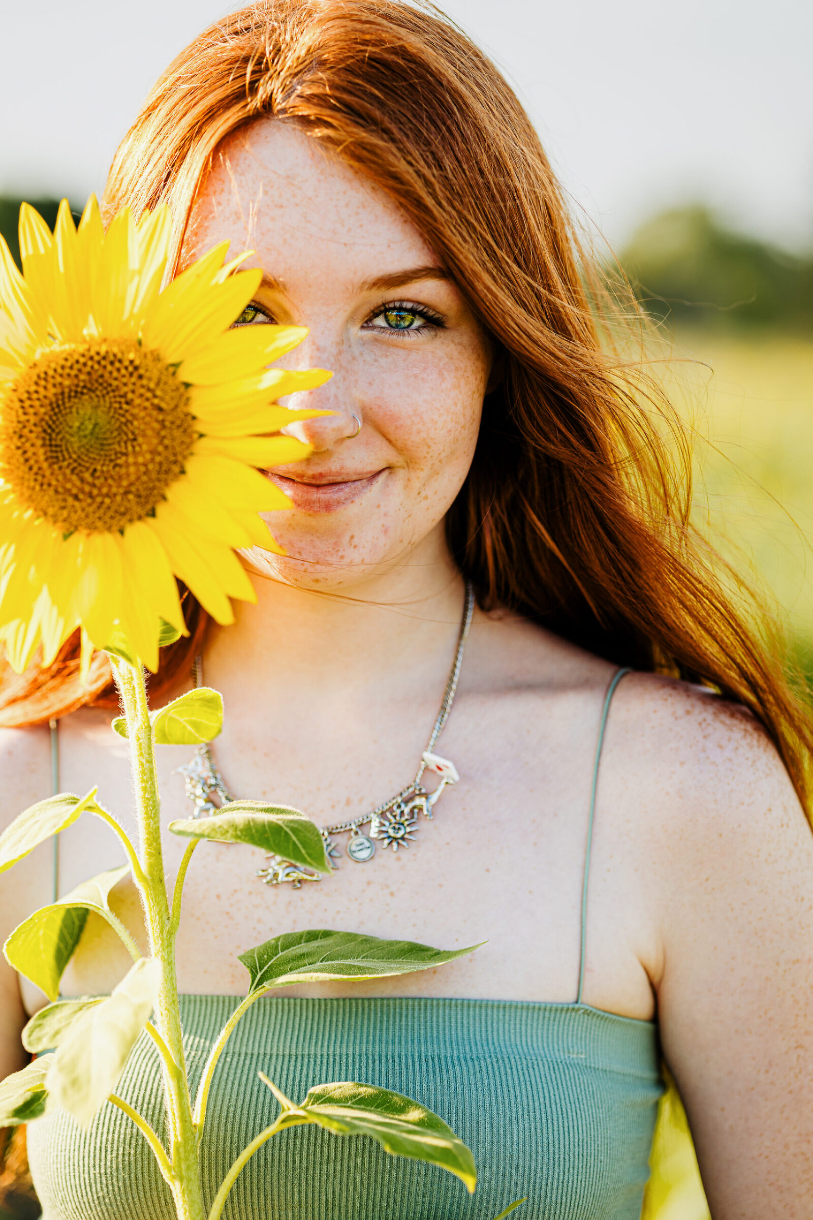 Teen girl with red hair and sage green top holding a giant sunflower.