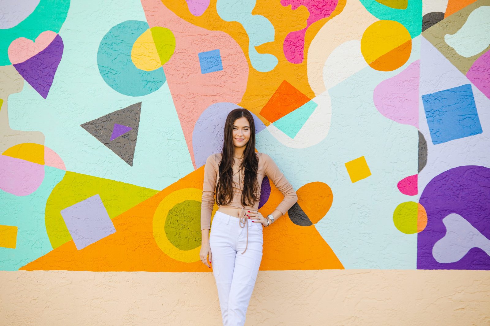 teen girl with long hair and white pants standing in front of colorful mural