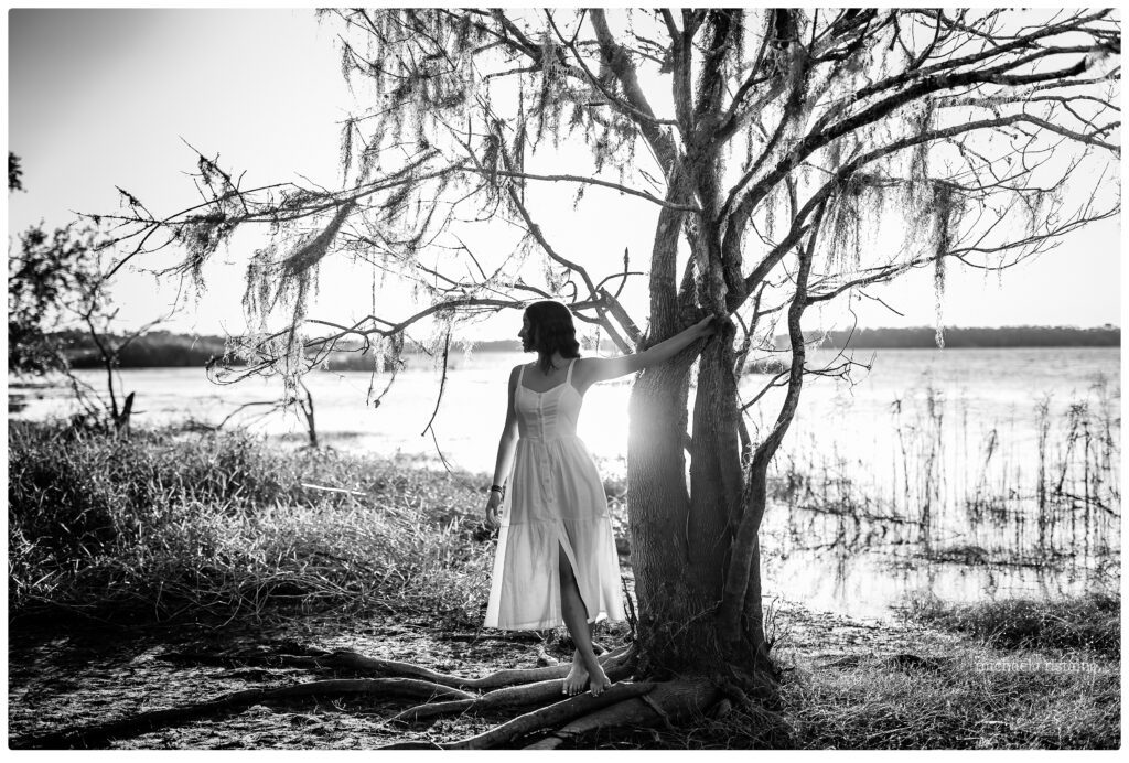 silhouette of teen girl in white dress holding onto a tree branch during sunset