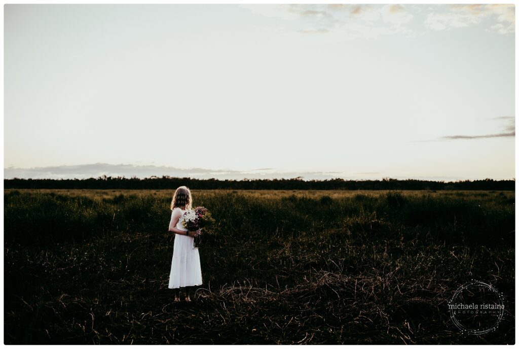 Senior silhouette standing in vast grassy field at golden hour in Sarasota.