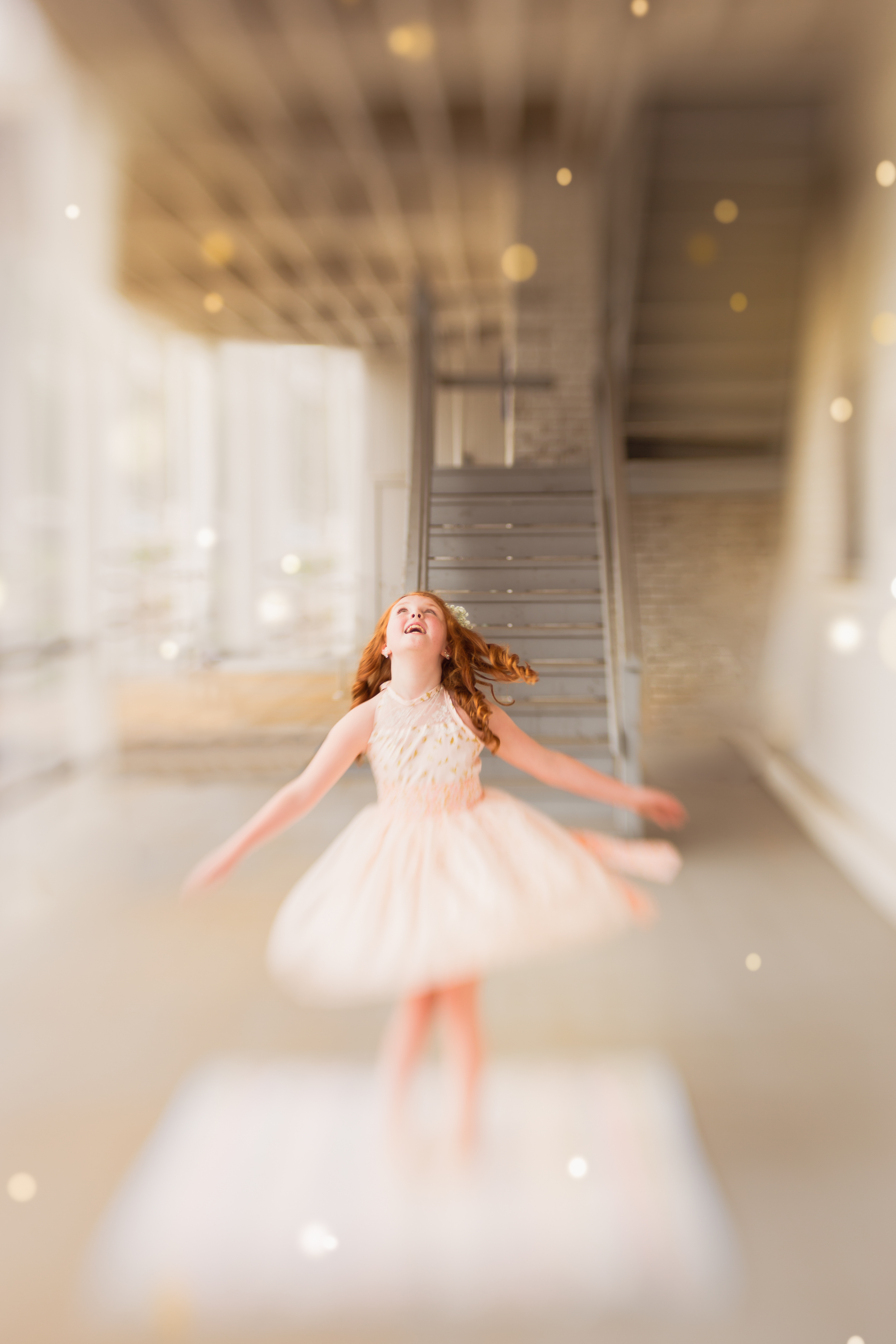 Young redheaded girl in a soft pink dress spinning joyfully in natural light — the beginning of a 10-year senior photo journey in Sarasota.