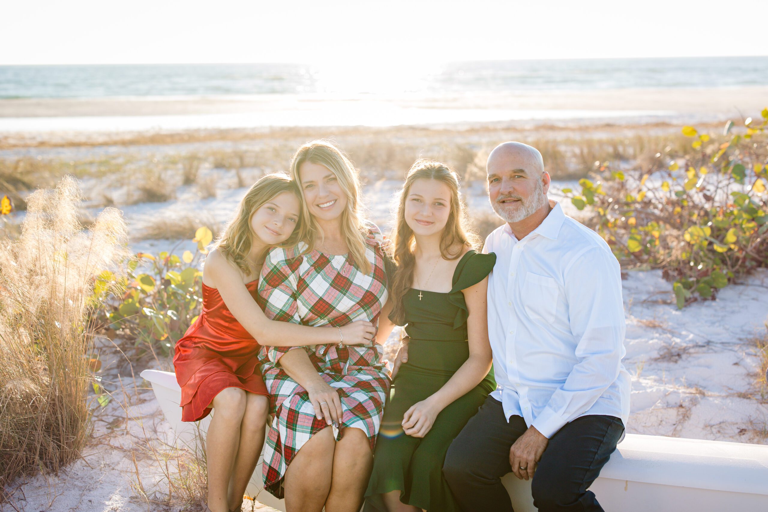 Family of four sitting together on the beach during a Sarasota holiday mini session, smiling at sunset.