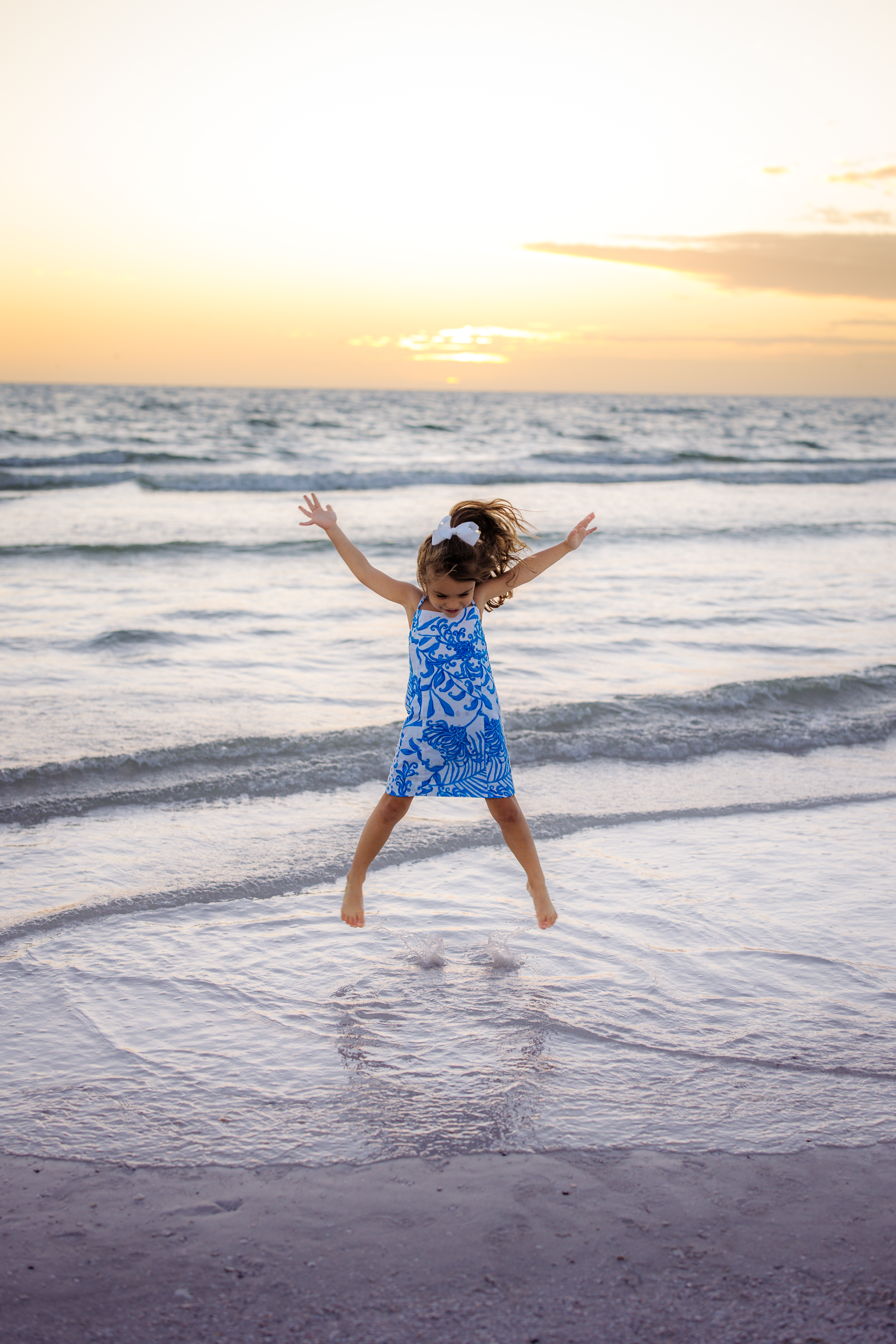 Little girl jumping with arms raised while playing at the beach during a Sarasota family photo session