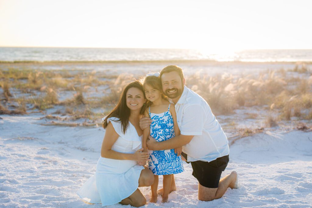 Smiling family kneeling together on Siesta Key Beach during a golden hour Sarasota family photo session