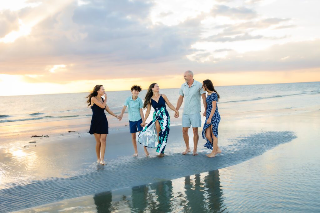 Family of five laughing and walking barefoot along the shoreline during a Sarasota beach photo session at sunset