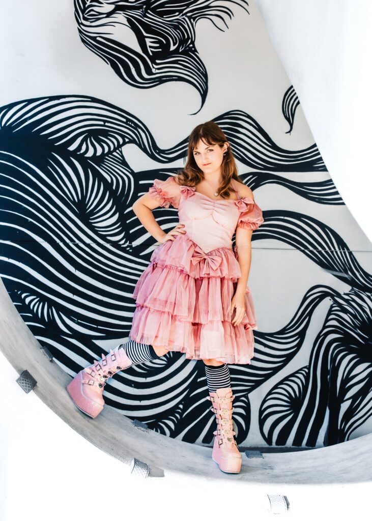 High school senior in pink taffeta dress and sparkle platform boots posing in front of black and white street mural in downtown Sarasota during senior portrait session
