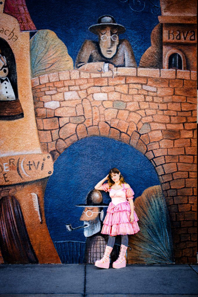 High school senior in pink ruffle dress and platform boots standing in front of colorful illustrated street mural in downtown Sarasota during senior portrait session