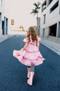 High school senior in pink ruffle dress skipping away down a downtown Sarasota street during senior portrait session
