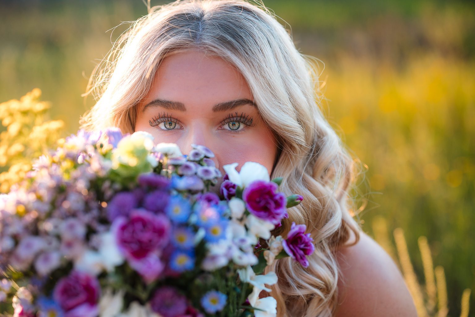 Close up senior portrait at Myakka River State Park Sarasota Florida, girl with green eyes peeking over colorful wildflower bouquet in golden light
