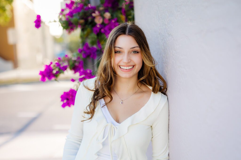 enior portrait in downtown Sarasota Florida, girl in cream ruffle top laughing against white wall with purple bougainvillea, Michaela Ristaino Photography