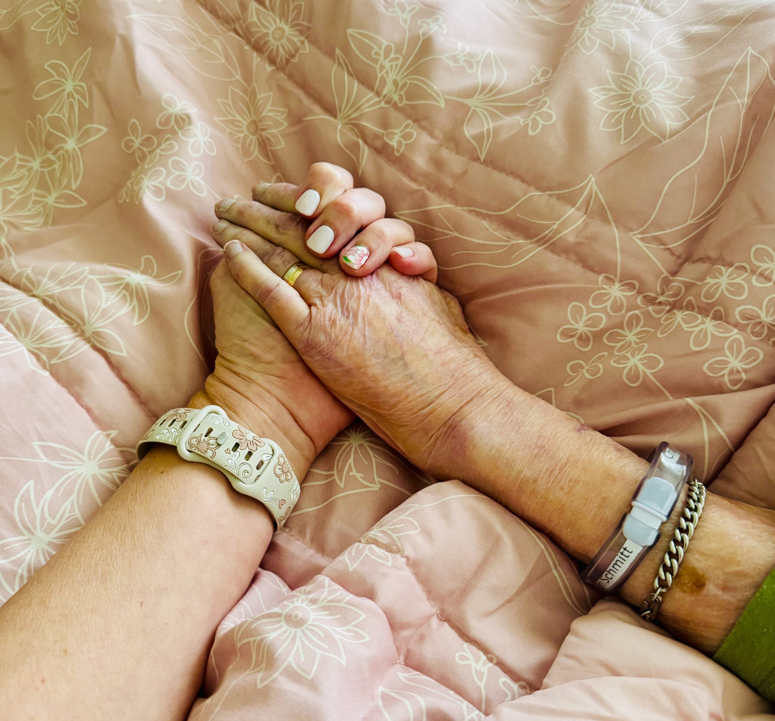 A daughter holds her mother's hand during her final days, a tender moment of love and presence.