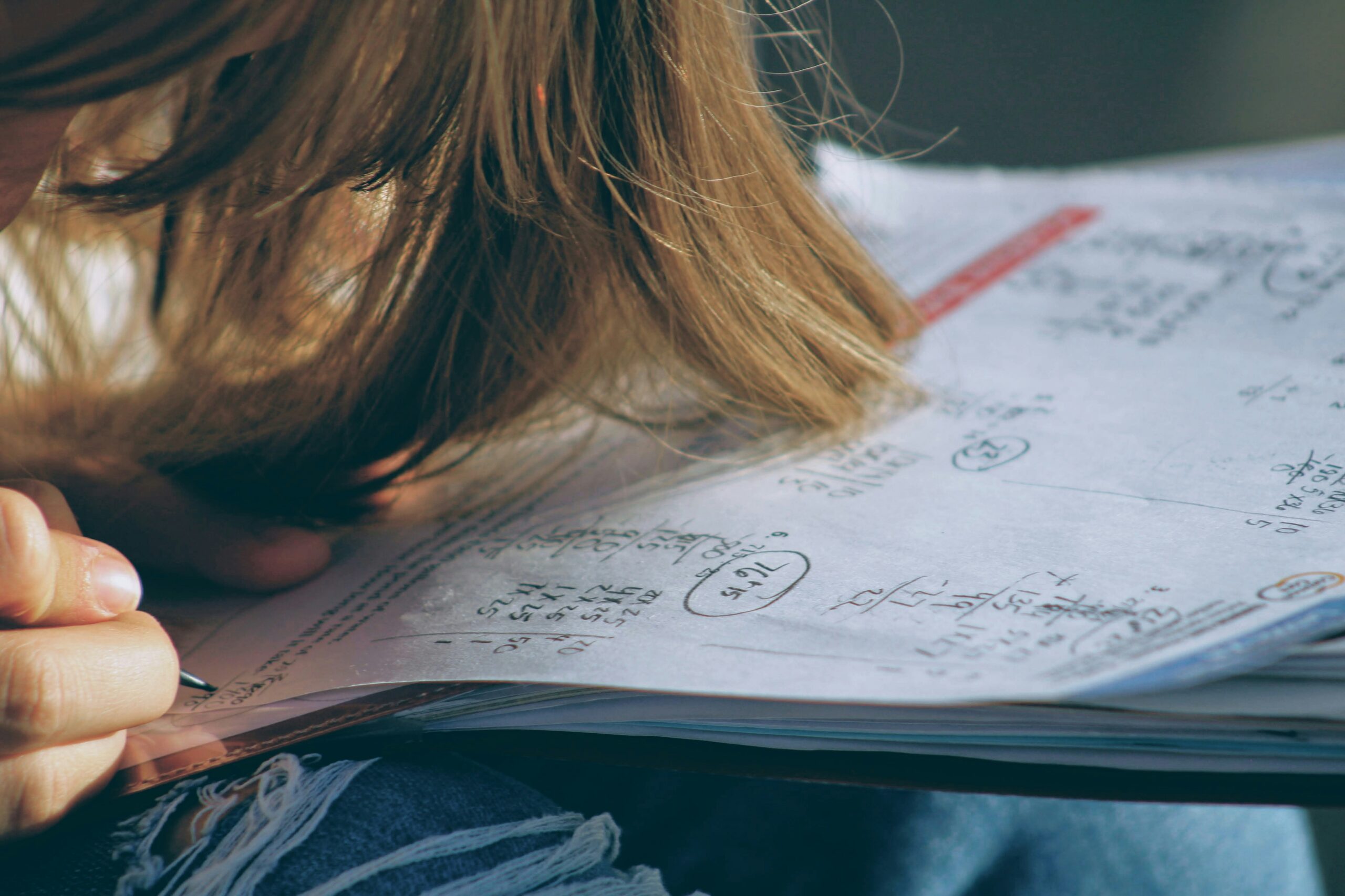High school senior doing homework, hair falling forward in concentration, capturing an everyday senior year moment