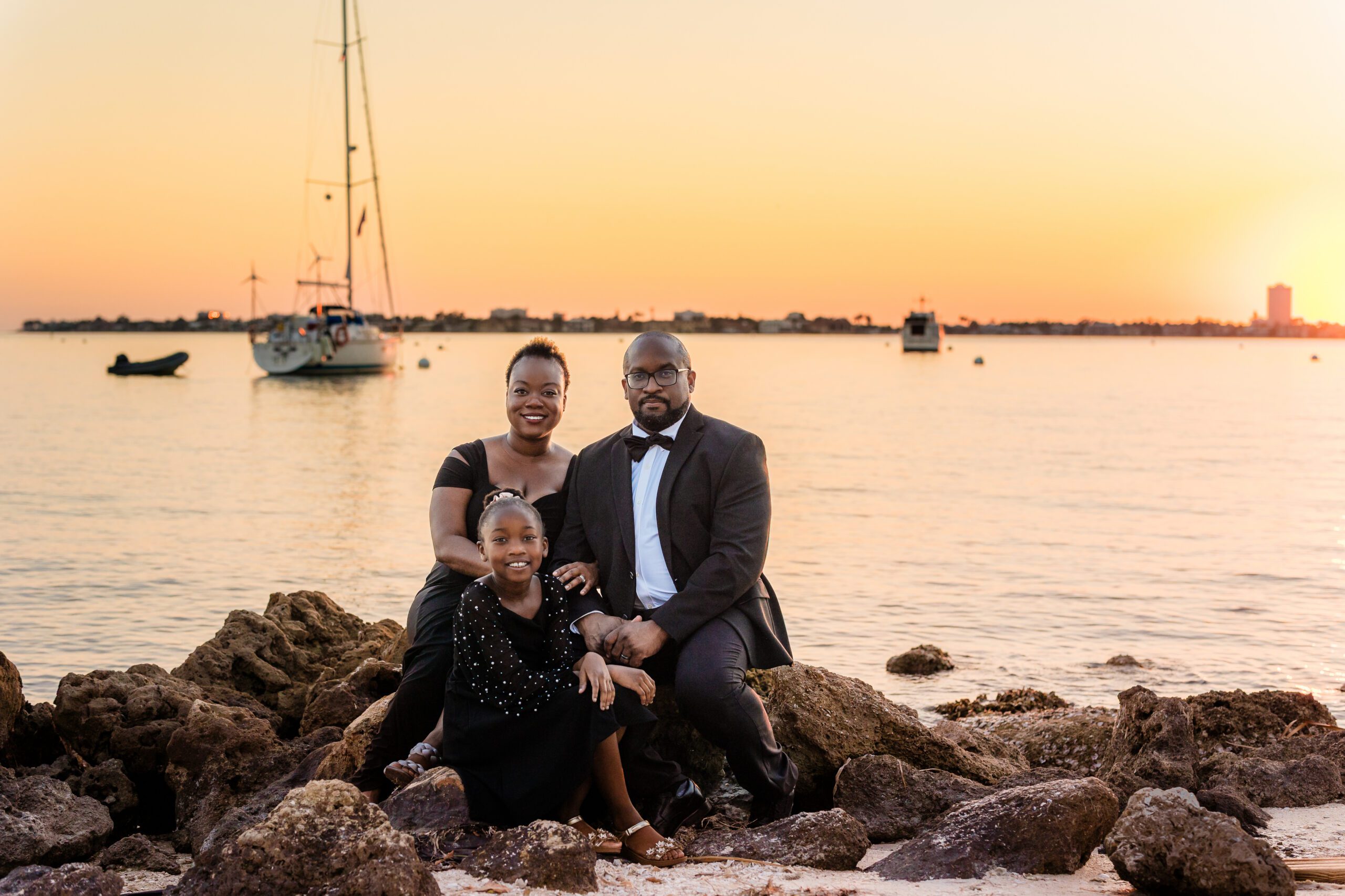 Family in black tie attire on rocks at sunset by the water