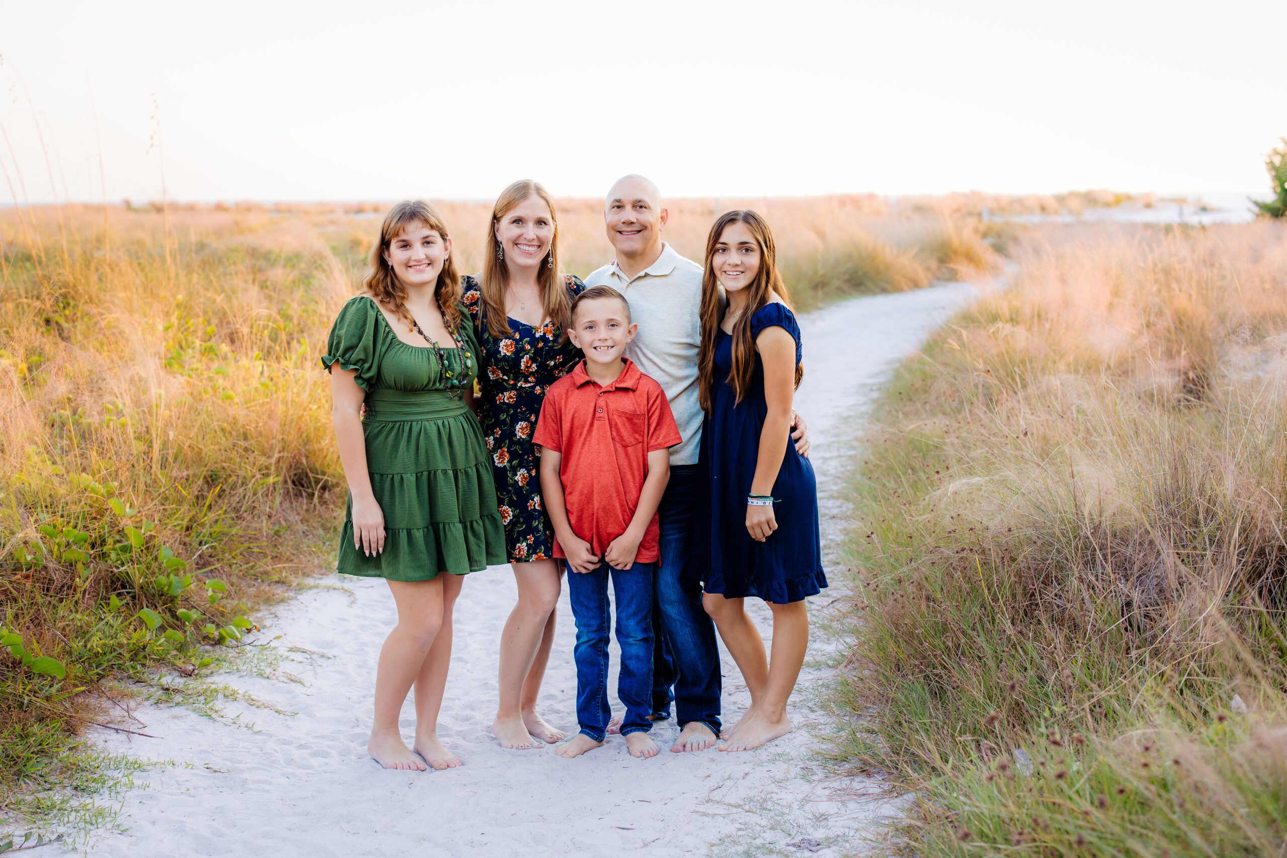 Family of five smiling on sandy beach path in Sarasota